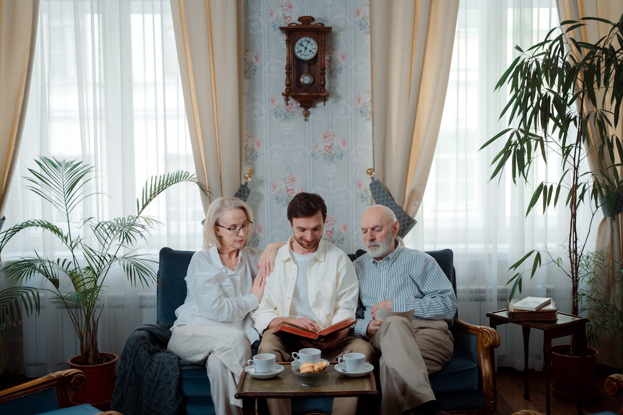 Elderly couple with son enjoying a photo album at home, sharing memories.
